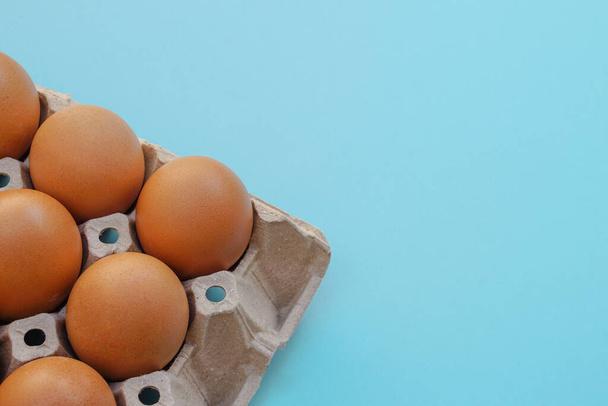 Chicken raw eggs in paper egg panel or in an egg stall on blue background. - Foto, Bild
