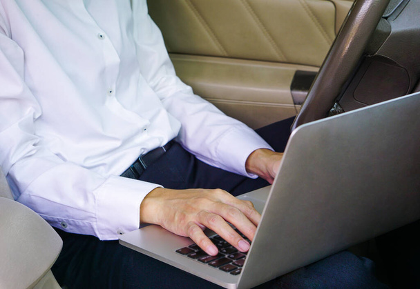 Бизнесмен работает на ноутбуке, сидя на водительском сидении в машине. Концепция образа жизни. - Фото, изображение
