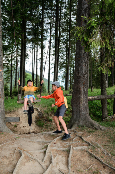 A boy swings on a swing somewhere in the forest, a walk in the Carpathians in the summer. - Valokuva, kuva