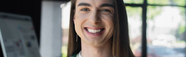 Cheerful nonbinary designer looking at camera in creative agency, banner  - Foto, Imagem