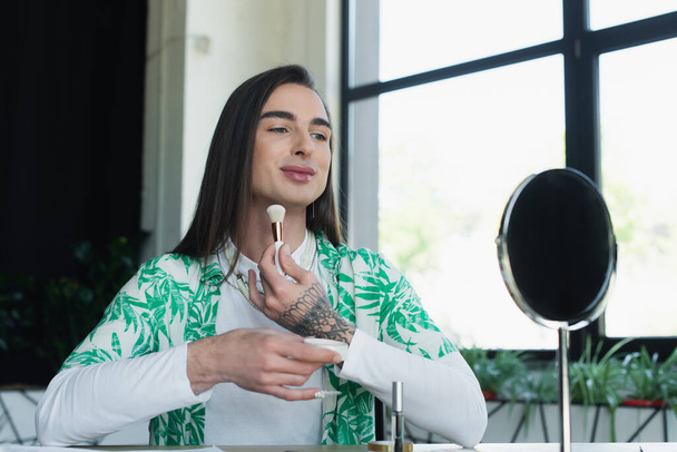 Smiling queer person holding face powder near mirror in creative agency  - Foto, immagini