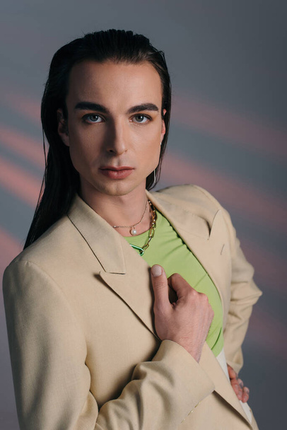 Young nonbinary person in jacket looking at camera on abstract background  - Foto, Imagen