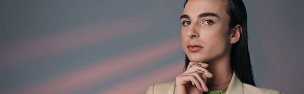Young queer model touching chin and looking at camera on abstract background, banner  - Foto, Bild