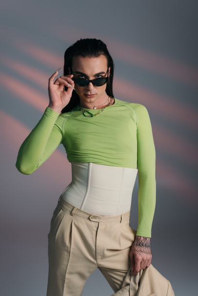 Young queer model holding sunglasses and jacket on abstract background  - Foto, imagen
