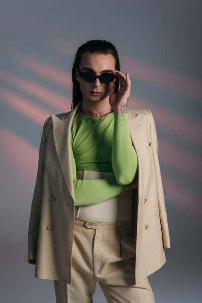 Trendy nonbinary person in sunglasses and suit standing on abstract background  - Photo, image