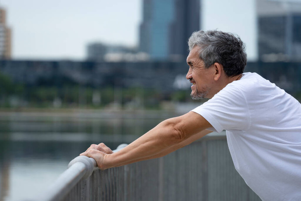happy senior man with grey hair warming up before workout in the city park. concept for elderly people lifestyle, health care, wellbeing - Φωτογραφία, εικόνα