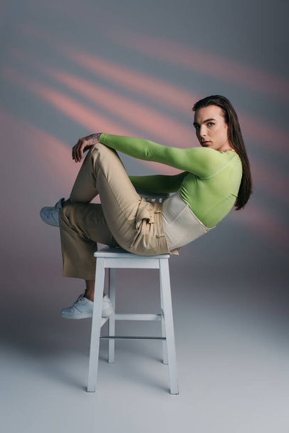 Stylish queer model posing on chair on abstract background  - Fotografie, Obrázek