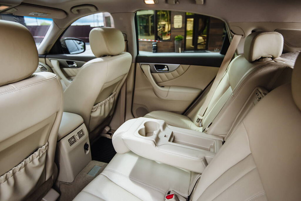 Πολυτελές εσωτερικό αυτοκινήτου από λευκό δέρμα. Δερμάτινο αναδιπλούμενο μπράτσο μπράτσο με ποτηράκια στα πίσω καθίσματα ενός οχήματος. Καθαρό δερμάτινο εσωτερικό: λευκά πίσω καθίσματα, προσκέφαλα και ζώνες. - Φωτογραφία, εικόνα