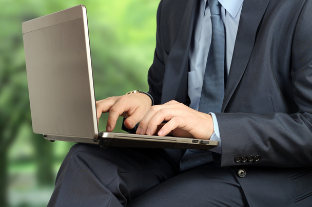 Молодой бизнесмен, работающий с ноутбуком, сидит снаружи, метр
 - Фото, изображение