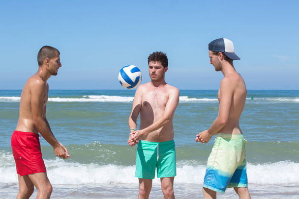 group of teenage friends playing volleyball on beach - 写真・画像