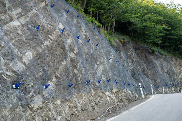 Reinforcing mountain slope with metal mesh and concrete reinforcement, preventing rocks falling on the road. Landslide and rock sliding prevention in Georgia. Cliff erosion control concept.  - Foto, imagen