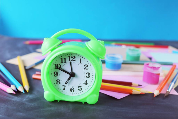 Alarm clock on the table, against the background of multi-colored paper, books and stationery, back to school, education, table for schoolchildren - Valokuva, kuva