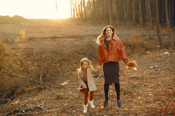 Modna matka z córką. Rodzina w jesiennym parku. Córeczka w brązowym płaszczu. - Zdjęcie, obraz