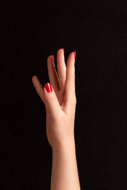Female hand with beautiful manicure - red nails on dark black background - Foto, immagini
