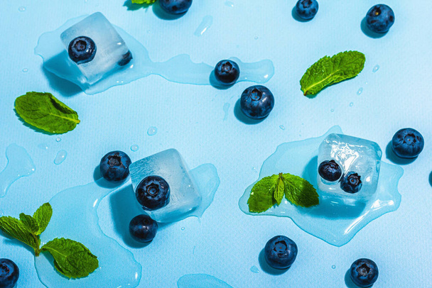 Blueberry, mint, and ice cubes. A trendy hard light, dark shadow, fresh summer blue background, flat lay, top view - Foto, Imagen