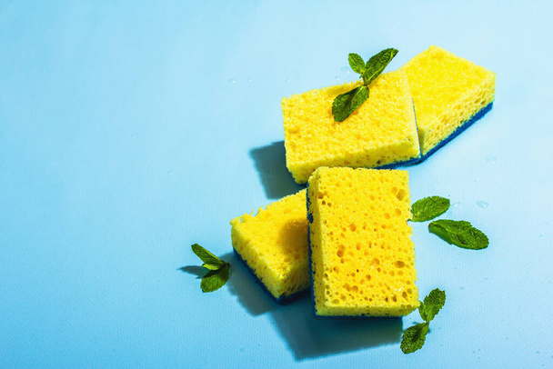 Bright yellow sponges for washing dishes. Organic cleaning concept, minty freshness. A trendy hard light, dark shadow, blue background, flat lay, copy space - 写真・画像