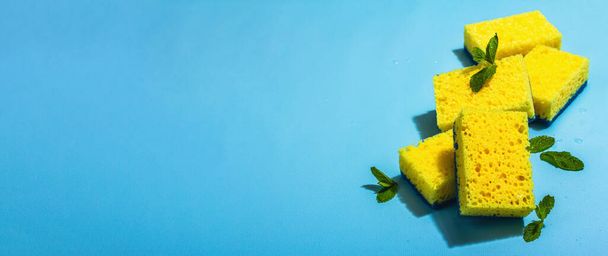 Bright yellow sponges for washing dishes. Organic cleaning concept, minty freshness. A trendy hard light, dark shadow, blue background, flat lay, banner format - Valokuva, kuva