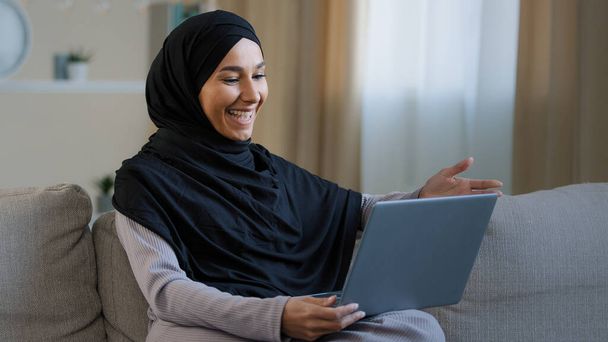 Friendly arabian muslim woman girl in hijab sit on cozy sofa talk video call with friend greeting at computer webcam take interview distance virtual communication in social networks use wi-fi at home - Valokuva, kuva
