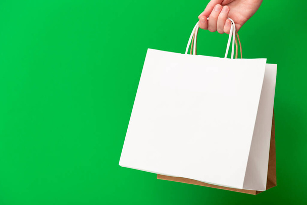 Yeşil arka planda iki alışveriş çantası tutan kadın. Beyaz ve kahverengi el işi boş kağıt torbaları. Kara Cuma indirimi, indirim, alışveriş ve ekoloji konsepti - Fotoğraf, Görsel