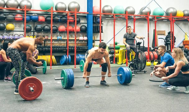 Сильний чоловік практикує важку атлетику в спортзалі зі своїми партнерами, вітаючи його
 - Фото, зображення