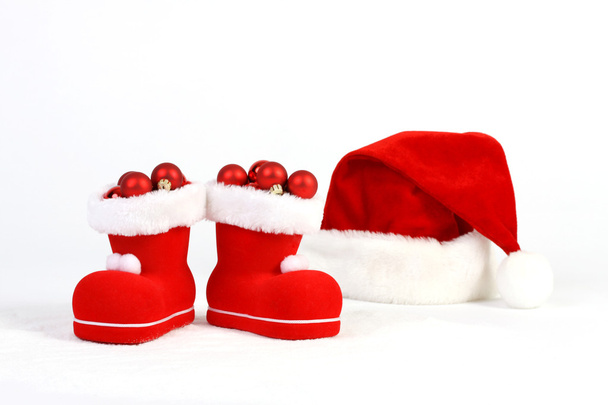 Santa Claus hat and boots with red and matt christmas balls on snow in front of white background - Фото, зображення