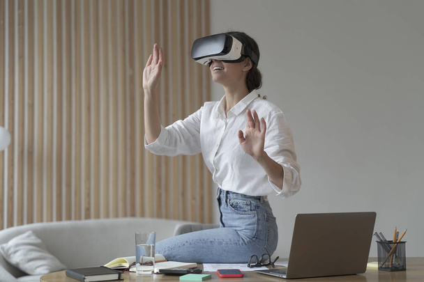 Employee experience with virtual reality. Impressed business woman sitting on office table, using vr glasses goggles at work, testing innovative method for business, interacting with digital interface - Photo, Image