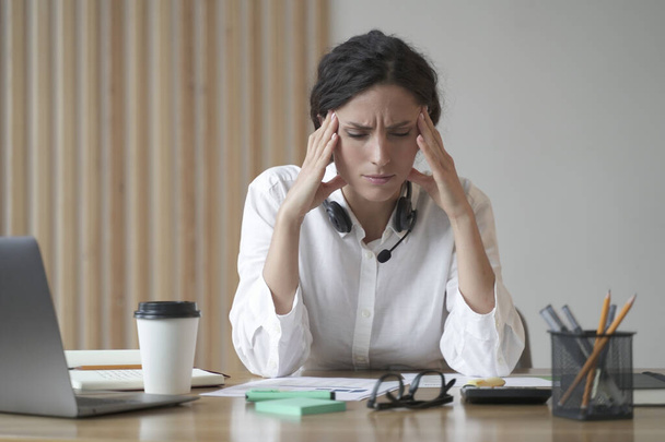 Gestresste junge Unternehmerin, die unter Kopfschmerzen leidet, die Schläfen massiert, während sie zu Hause im Büro sitzt, müde Freiberuflerin, die sich unwohl fühlt, den Kopf berührt. Migräne, Müdigkeit, Stress - Foto, Bild
