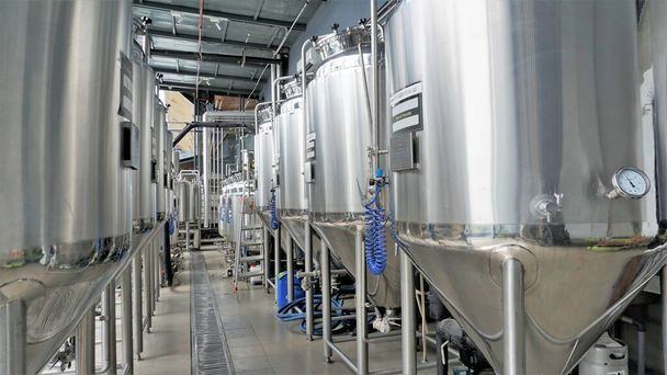 Row of shiny metal micro brewery tanks or Fermentation mash vats in Brewery factory. Modern beer plant with brewering kettles, tubes and tanks made of stainless steel - Foto, Bild