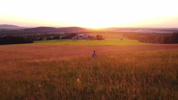 Thoughtful man in a colourful shirt walks in the early evening light through a meadow teeming with life and biodiversity, wondering how to preserve this healthy ecosystem. - Materiał filmowy, wideo