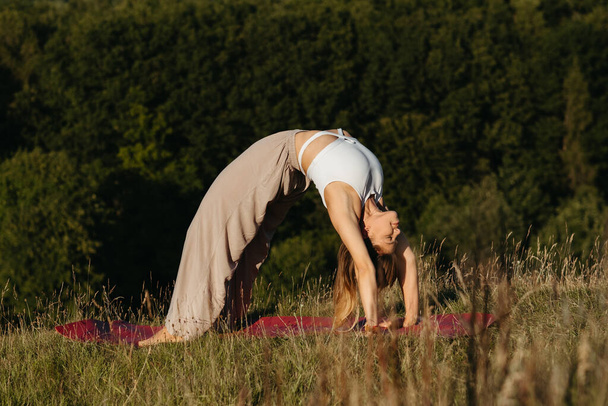 Молодая женщина делает упражнения моста во время йоги на открытом воздухе с красивым фоном - Фото, изображение