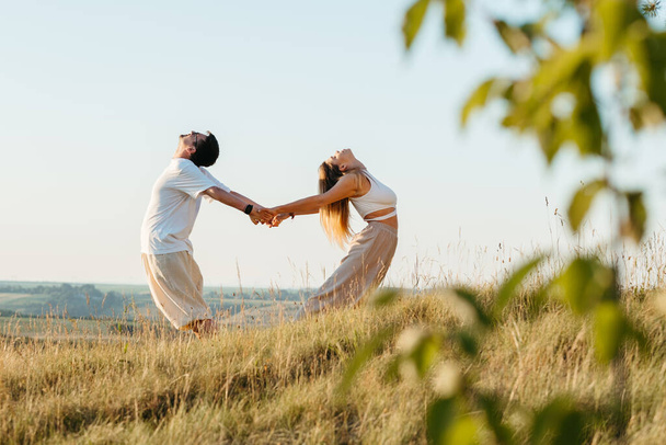 Young Adult Couple Making Beautiful Pose, Man and Woman Practicing Yoga Outdoors with Scenic Landscape on the Background at Sunset - Foto, Imagem