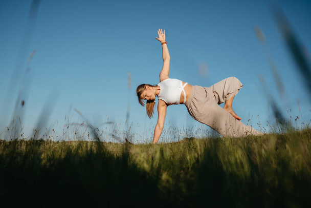 Young Woman Practicing Yoga Outdoors in the Field with Blue Sky on Background - Фото, зображення