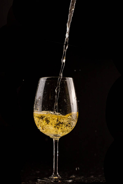 Белый бокал вина, с вином падает на черном фоне - Фото, изображение