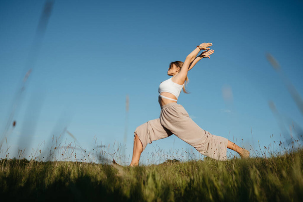 Young Woman Practicing Yoga Outdoors in the Field with Blue Sky on Background - Φωτογραφία, εικόνα