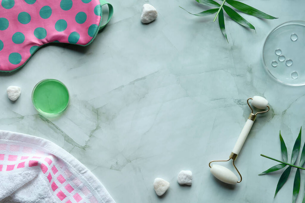 White stone facial roller. Facial anti-age massage for natural lifting treatment. Beauty concept, flat lay on mint green with palm leaves. Towel, sleep mask, moisturizer in petri dishes. - Foto, Imagen
