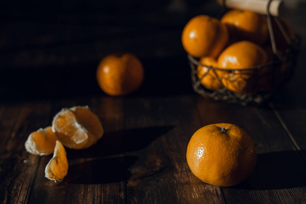 individual tangerines and a basket of tangerines on a dark wooden table - Foto, imagen