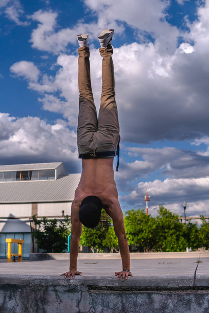 An athletic Latin man in the park training carrying his body with his arms. Hispanic man doing outdoor handstand training. Man from behind lifting his weight with his hands. - Photo, image