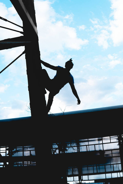Black silhouette of a man climbing a metal structure. Black man doing an extreme activity. Silhouette of a man on top of a tower posing with the sky in the background. - Photo, image