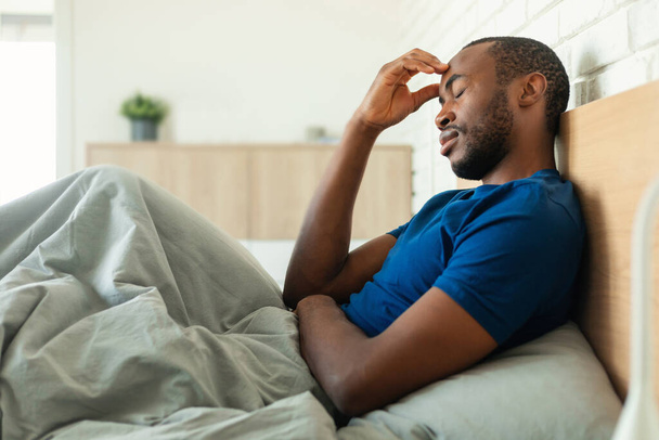African American Man Having Headache Touching Forehead Suffering From Pain With Eyes Closed Sitting In Bed In Modern Bedroom At Home. Male Health Problem, Migraine Symptom, Side View - Foto, Imagem