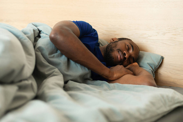 African American Guy Sleeping Under Gray Blanket Lying In Bed In Modern Bedroom At Home. Man Napping Resting Head On Pillow Holding Hands Near Face. Selective Focus - Foto, immagini