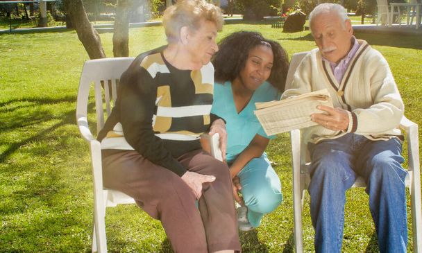 African nurse using tablet with elderly retired couple outdoor in the rehab hospital garden. Happiness, rehabilitation and retirement concept. - Foto, Bild