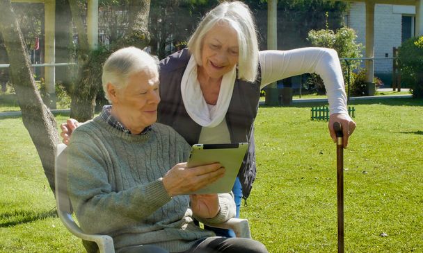 Boldog nyugdíjas pár használ tech kütyü szabadban egy napsütéses napon. - Fotó, kép