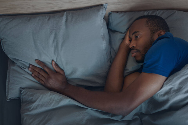 Unhappy Black Man Touching Pillow Lying In Bed Mourning Suffering From Loss Or Breakup Feeling Lonely In Modern Bedroom At Home At Night. Loneliness Problem, Divorce. Low Light Shot - Foto, afbeelding