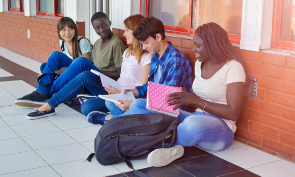 Multi compagni di scuola etnici seduti nel corridoio della scuola rilassarsi e fare lezione di scuola. - Foto, immagini