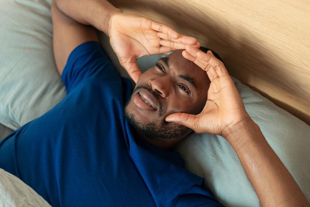 Вид зверху чорний хлопець страждає від головного болю, торкаючись досягнення голови лежачи в ліжку в сучасній спальні вдома. Мігрень Симптом і чоловічі проблеми здоров'я концепція
 - Фото, зображення