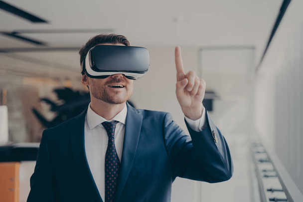 Новий досвід. Усміхнений здивований бородатий бізнесмен в 3d окулярах, використовуючи доповнену реальність в роботі, одягнений формально, вказуючи на об'єкт в інтерфейсі користувача. Сучасні технології та концепція бізнесу
 - Фото, зображення