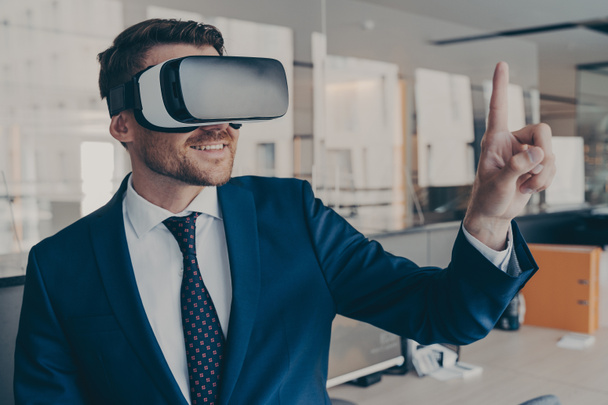 VR gözlük takan, 360 derecelik kulaklık kullanıcı arayüzü ile etkileşimde bulunan genç finansör, ofisinde dururken, 3D menüdeki içeriği seçer. - Fotoğraf, Görsel