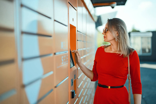 Kobieta odbiera pocztę z automatu samoobsługowego terminala pocztowego. - Zdjęcie, obraz