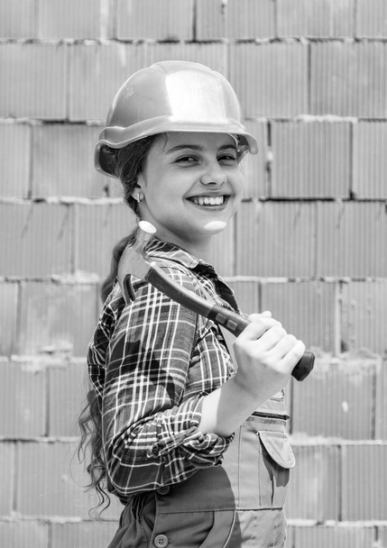 Repair concept. kid wear helmet on construction site. teen girl builder with building tool hammer. child on repairing work. concept of renovation in workshop. busy professional carpenter. - 写真・画像
