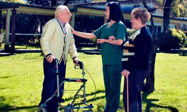 Joven asiática enfermera sonriendo al aire libre con ancianos jubilados pareja, hablando con ellos en el hospital jardín. - Foto, Imagen